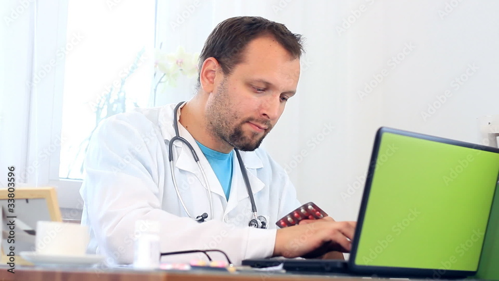 Male doctor working on computer and checking medications Male doctor working on computer and checking medications