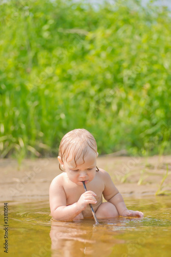 Adorable baby sit in river and play with sand and wood branch