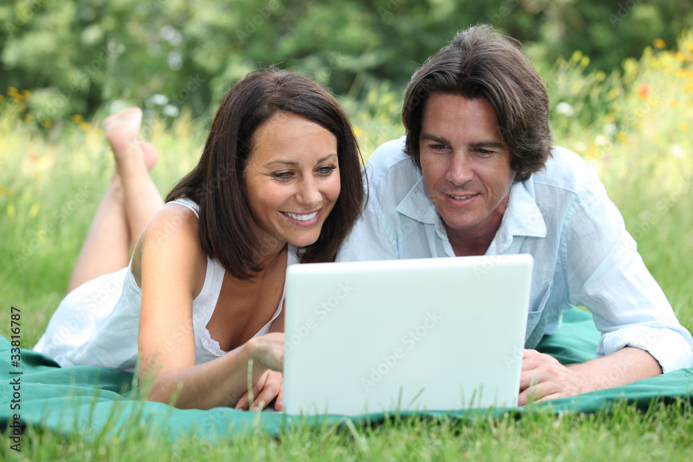 Couple lying on the grass looking at a laptop computer screen Couple lying on the grass looking at a laptop computer screen