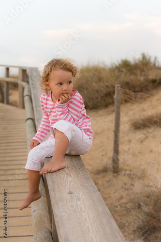 Little baby is seatting on the bridge and looking the ocean
