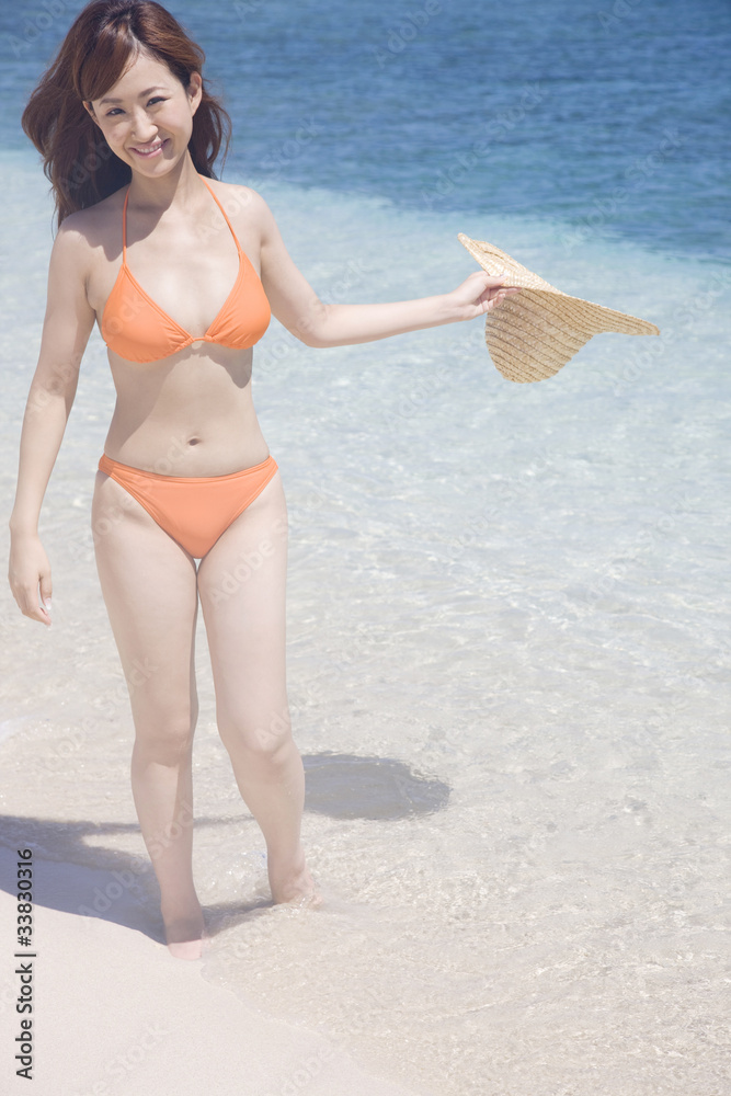 波打ち際で麦わら帽子を持つ水着女性 Stock Photo Adobe Stock
