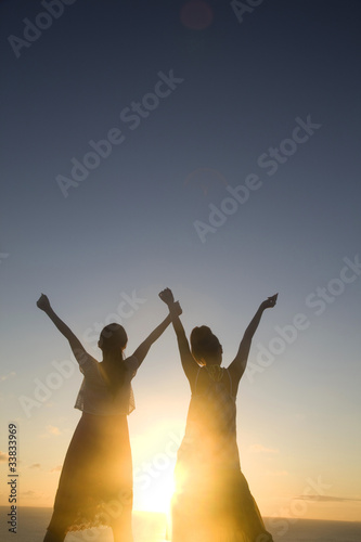 夕暮れに両手を空に広げる女性2人のシルエット