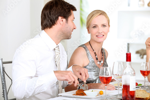 Couple sat at table eating meal and drinking wine
