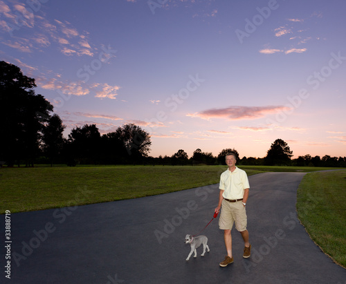 Senior man walking dog at sunset