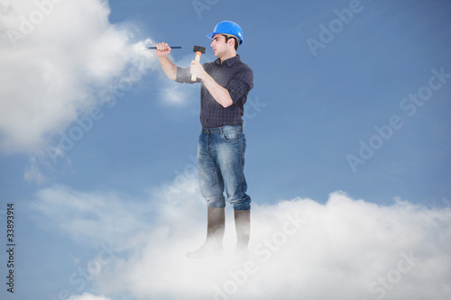 Photomontage of a workman driving a nail in the clouds © auremar