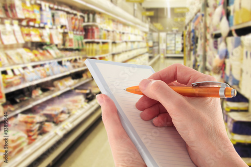 Hand with Pen Writing a Shopping List in a Supermarket