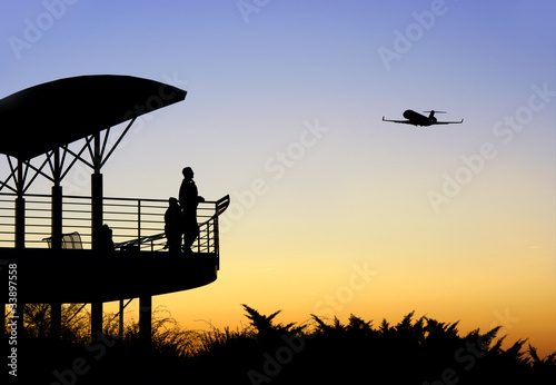 People in silhouette watching airplane take off