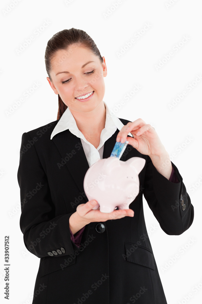 Beautiful woman in suit inserting a money bill in a pink piggy b Beautiful woman in suit inserting a money bill in a pink piggy b