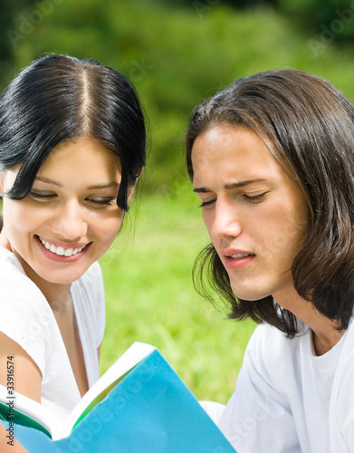 Young happy couple reading a book together, outdoors