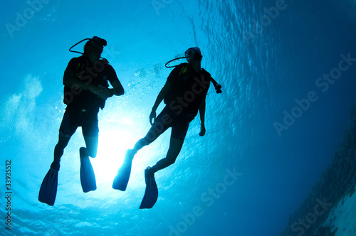 silouetted scuba divers on coral reef