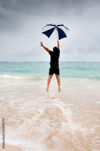 Tanned man jump with umbrella in blue sea under grey sky