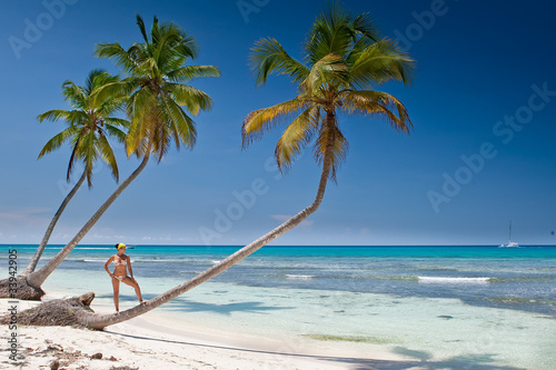 Tanned woman is standin on palm before blue sea