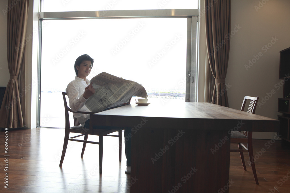 ダイニングテーブルで新聞を読む男性