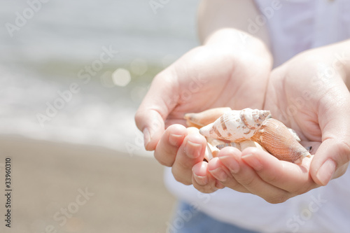 砂浜で貝殻を手に持つ女性