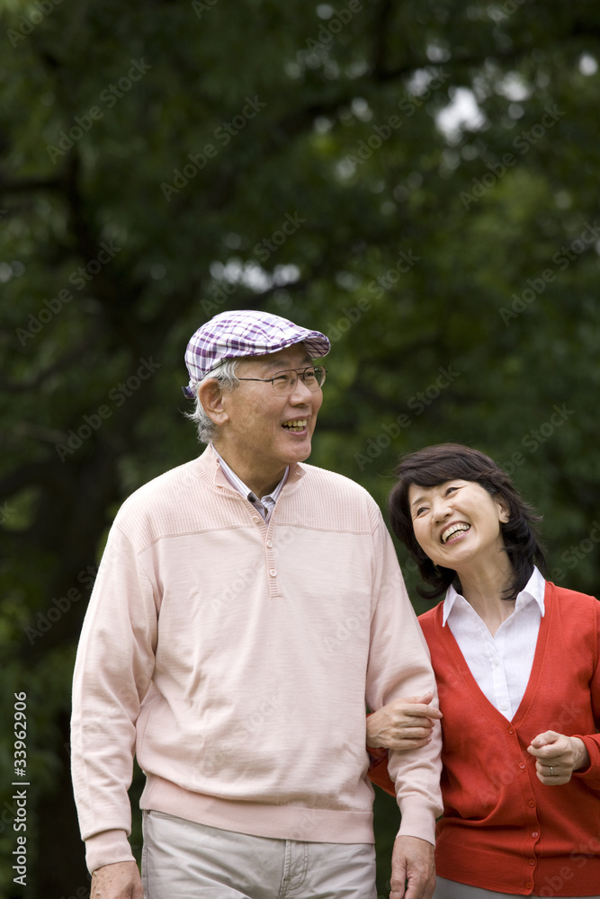 腕を組みながら公園を散歩する老夫婦 腕を組みながら公園を散歩する老夫婦
