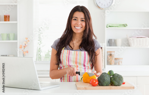 Beautiful woman relaxing with her laptop while cooking vegetable