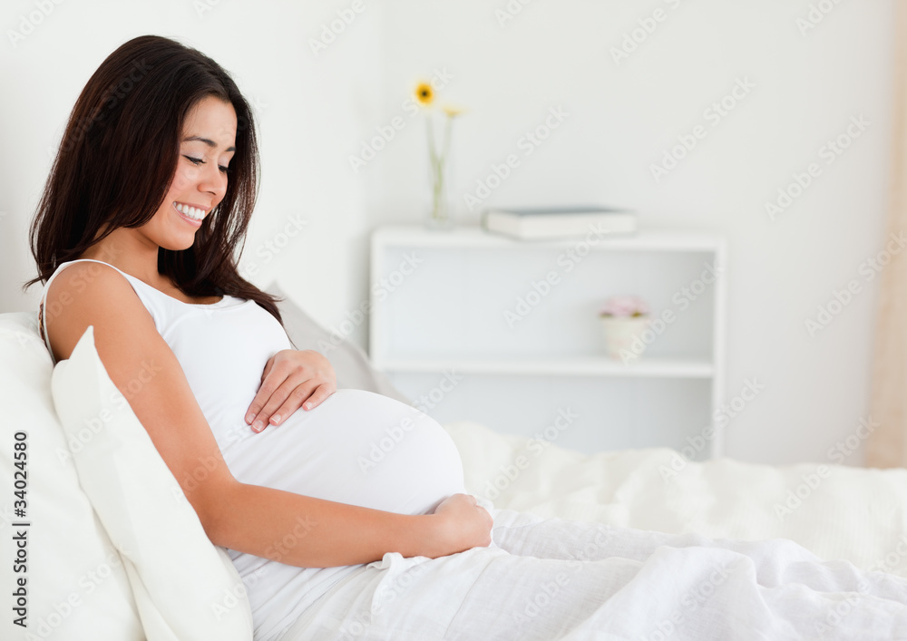Beautiful pregnant woman touching her belly while lying on a bed Beautiful pregnant woman touching her belly while lying on a bed