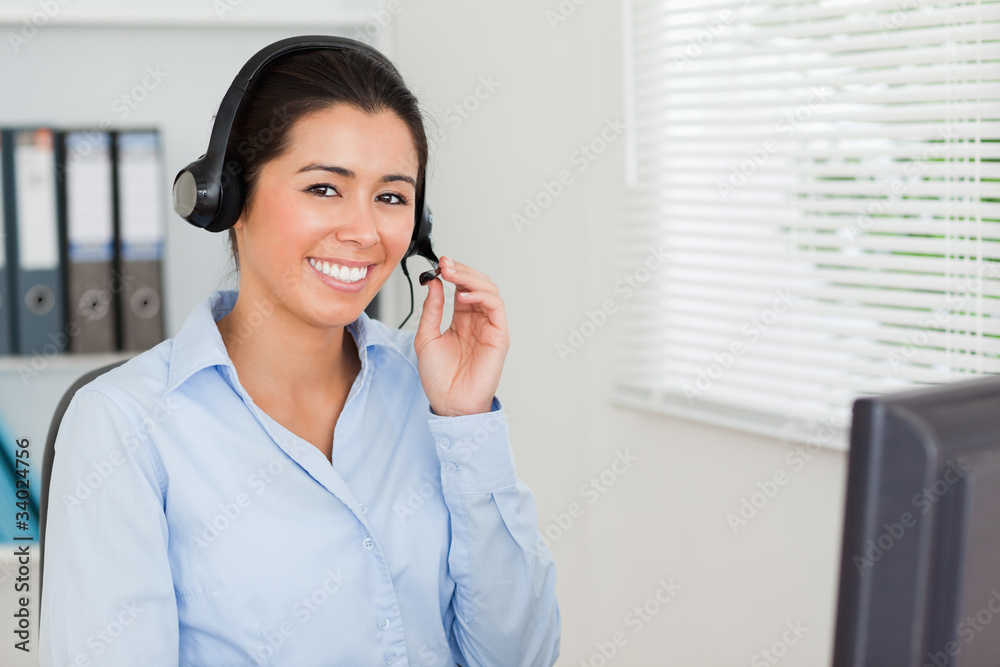 Charming woman with a headset helping customers while sitting Charming woman with a headset helping customers while sitting