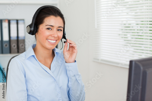 Charming woman with a headset helping customers while sitting
