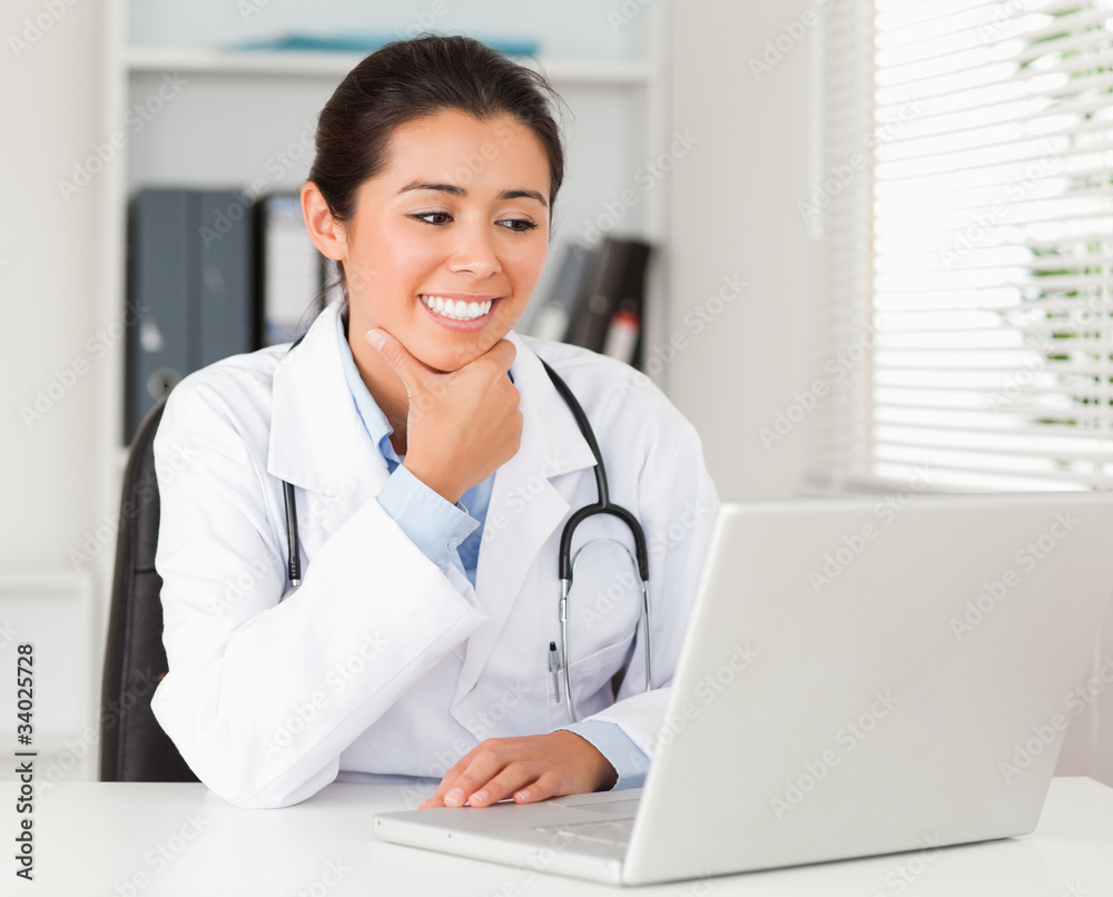 Attractive female doctor working with her laptop while sitting Attractive female doctor working with her laptop while sitting