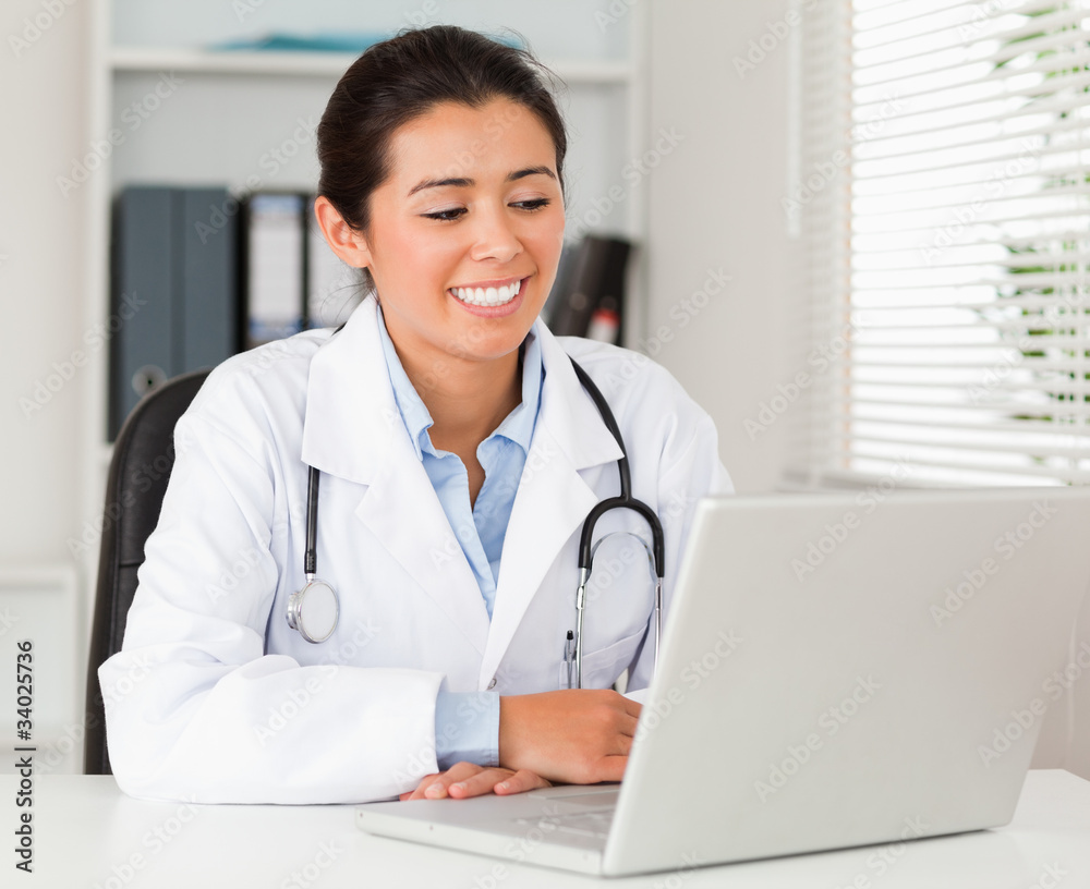 Good looking female doctor working with her laptop while sitting