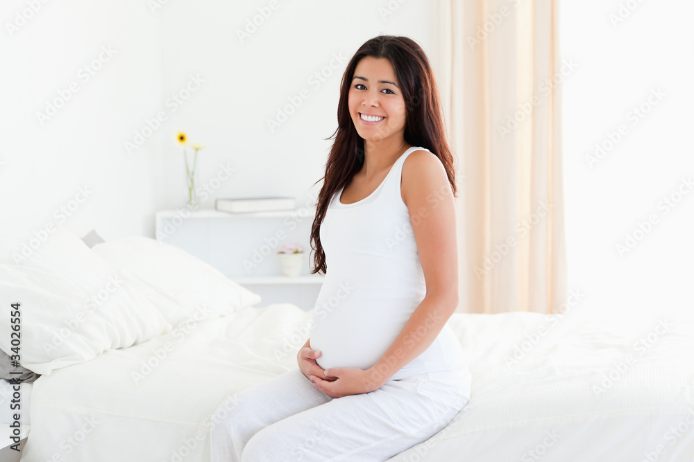 Beautiful pregnant woman touching her belly while sitting on a b