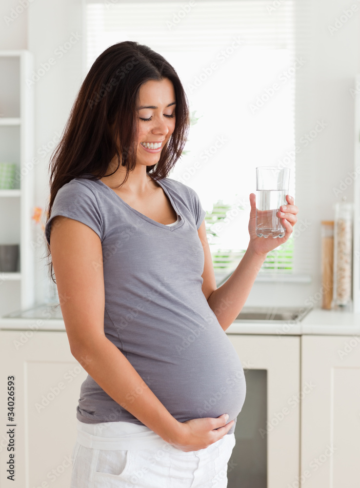 Charming pregnant woman holding a glass of water while standing