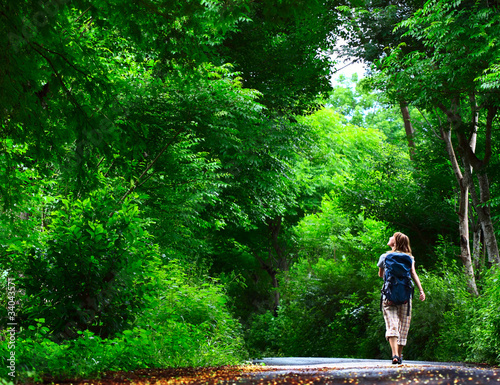 Young woman walking on green asphalt road in the forest