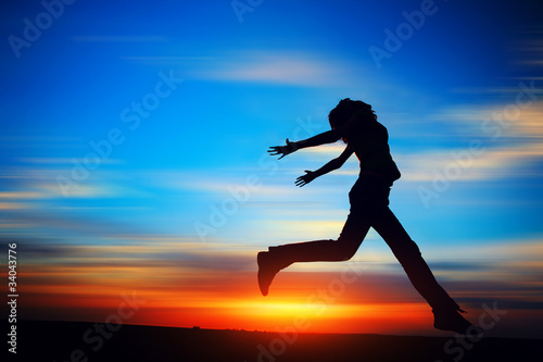 Young woman jumping on the meadow on motion blurred sunset background.