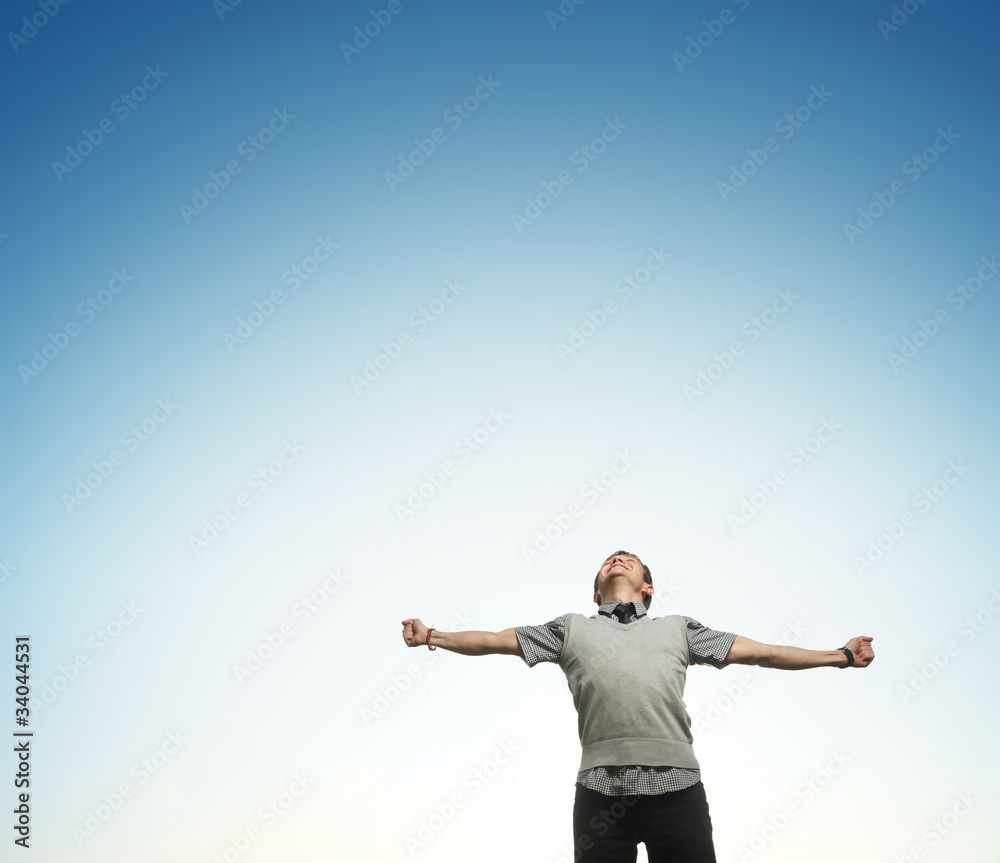 Young happy man on blue sky background with raising hands and looking to a sky Young happy man on blue sky background with raising hands and looking to a sky