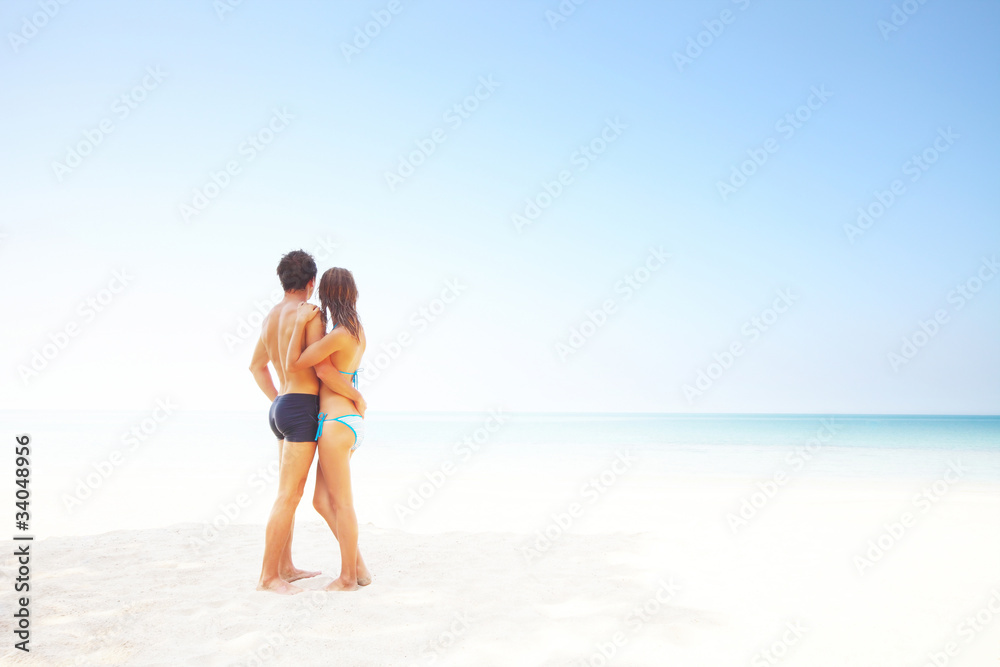 Young man and woman standing on warm sand at sunny day and enjoying each other
