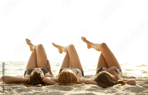 Three beautiful young girlfriends in bikini on the beach at sunr