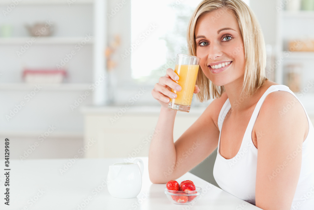 Woman sitting at a table toasting with orange juice looking into Woman sitting at a table toasting with orange juice looking into