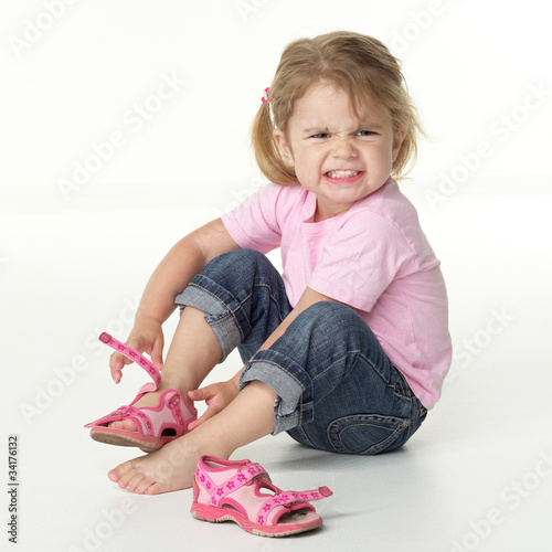 Adorable little girl is annoyed to put on her shoes photo