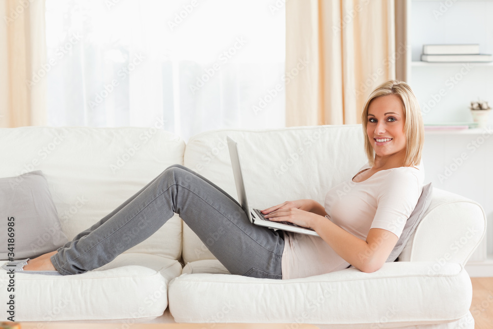 Cute woman with a laptop while lying on a sofa