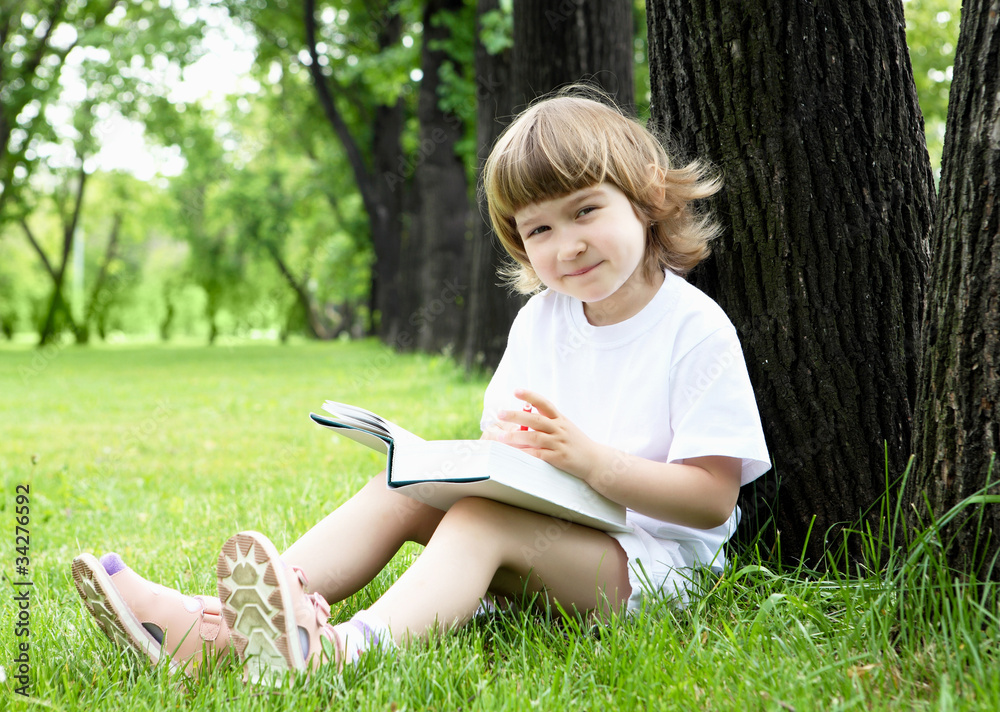Portrait of little girl reading a book in the park