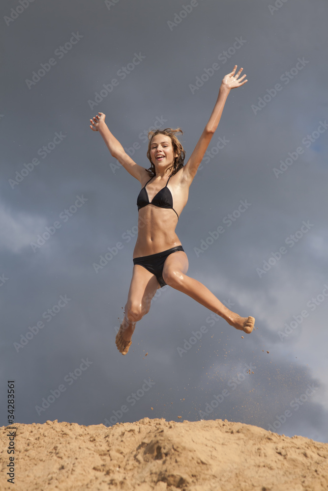 Young girl in swimsuit jumps above the sands embankment