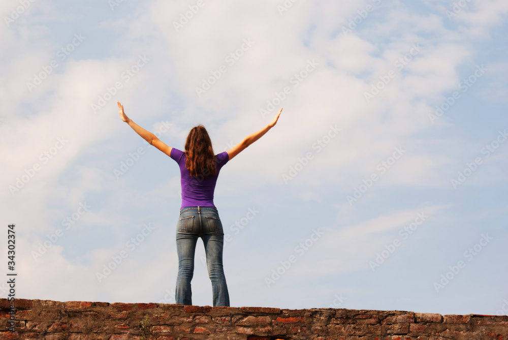 Young woman staying with raised hands against blue sky