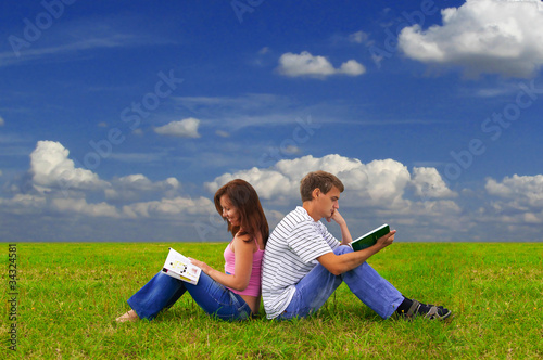 two teenagers studying outdoors on grass