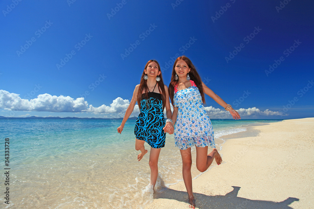 手をつなぎ笑顔で波打ち際を走る2人の女性