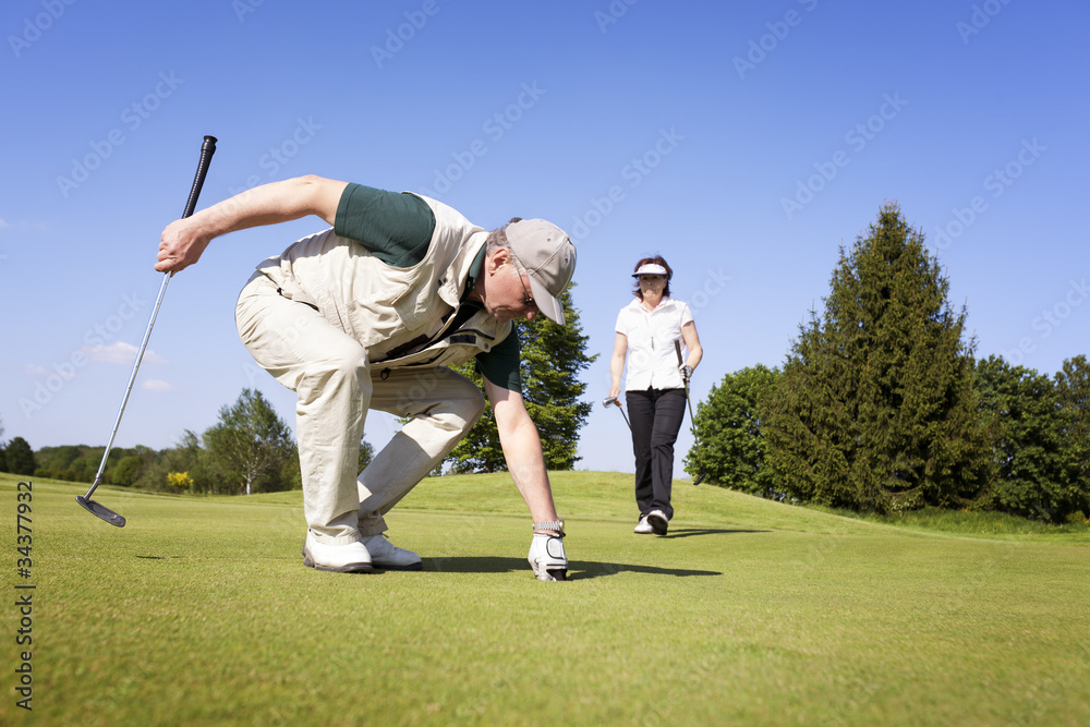 Obraz premium Golf player couple on green picking ball.