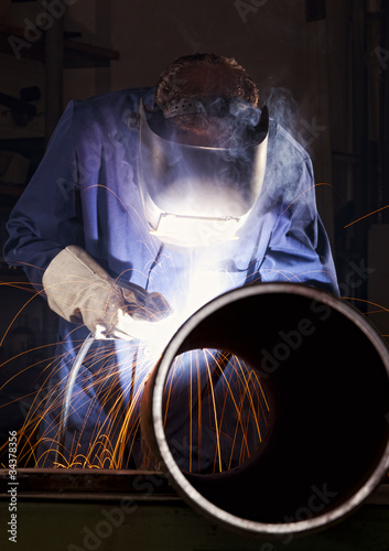 Worker welding pipe in workshop.