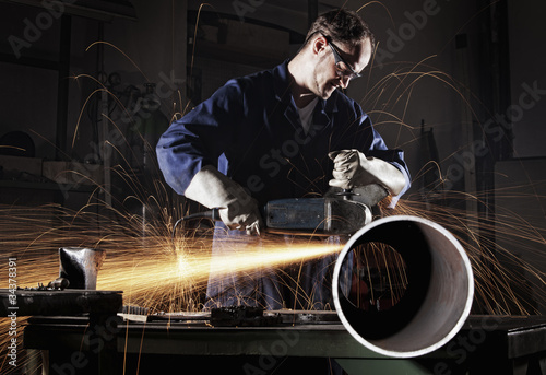 Worker cutting pipe with angel grinder. photo