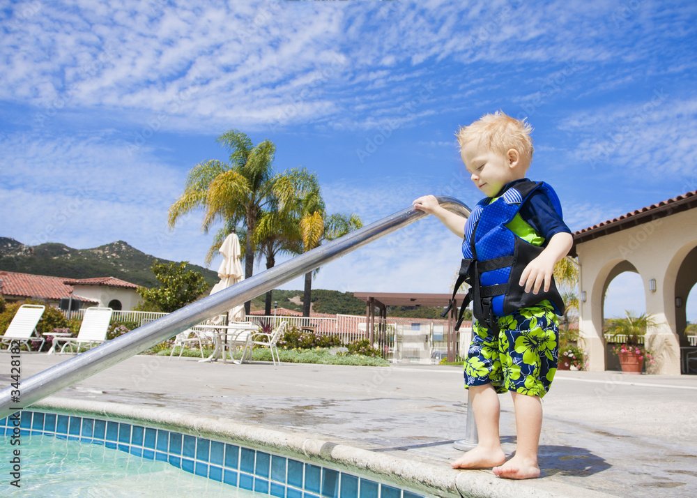 Naklejka premium Little Boy Cautiously Stepping into Outdoor Pool