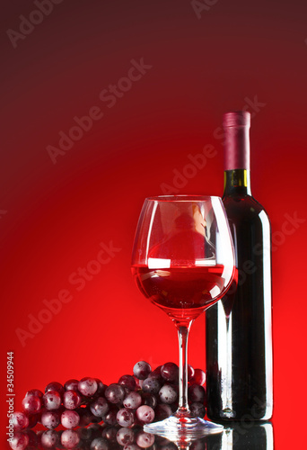 bottle of wine glasses and grapes on red background