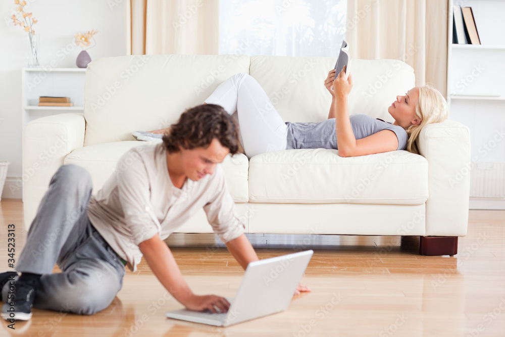 Man using a laptop while his wife is reading a book