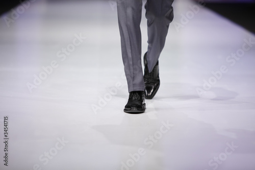Fotografi foot of male model in gray trousers and black shoes on catwalk