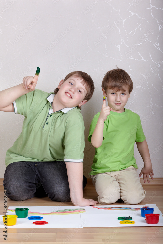Naklejka premium Two boys in green T-shirts sit on floor and draw