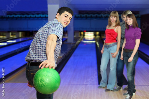 Young man prepares throw ball on path for bowling and three girl