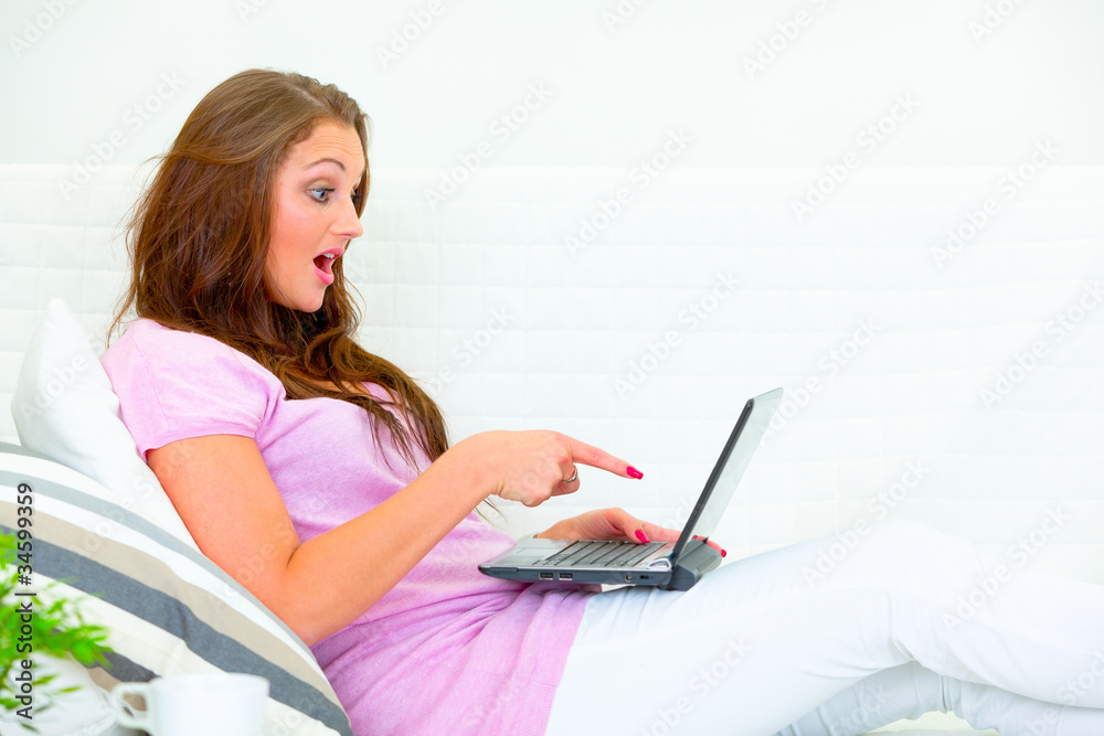 Confused pretty woman on couch and pointing finger at laptop Confused pretty woman on couch and pointing finger at laptop